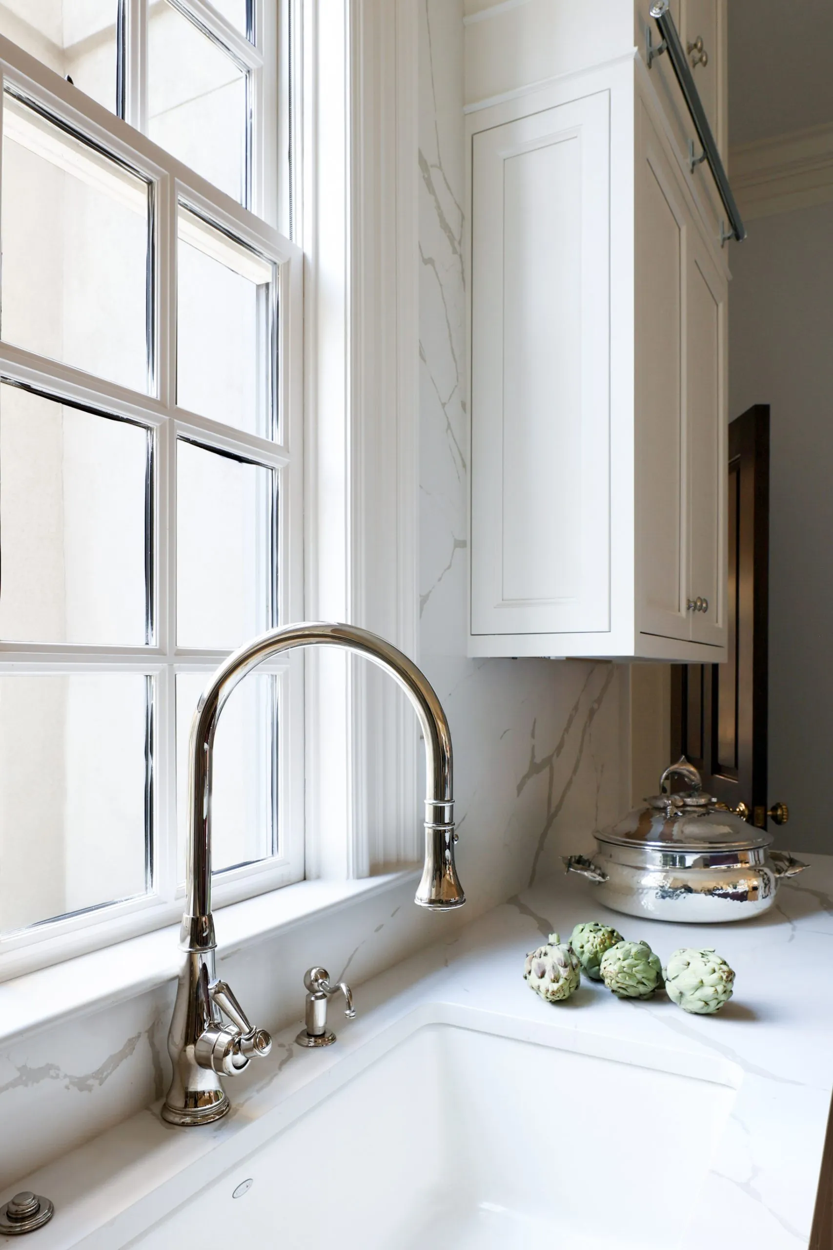 A polished nickel bridge faucet over a marble sink in front of a window